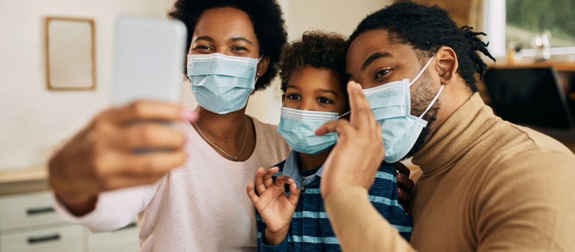 happy-african-american-family-with-face-masks-having-video-call-smart-phone-home (1) (1)