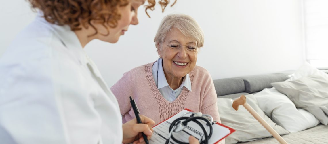 Senior woman is visited by her doctor or caregiver. Female doctor or nurse talking with senior patient. Medicine, age, health care and home care concept. Senior woman with her caregiver at home